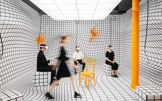 Four people wearing VR headsets in a room with grid-like walls and floors.