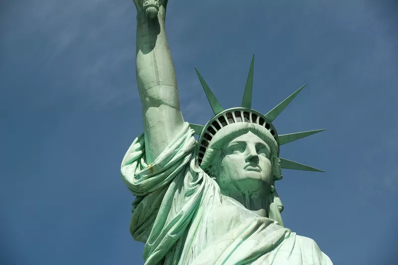 A close-up of the Statue of Liberty's head, arm, and torch with a blue sky in the background.