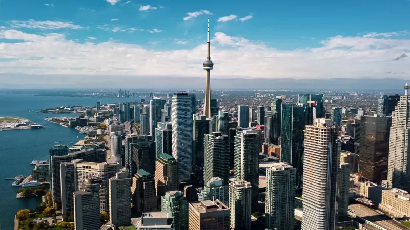Toronto skyline with the CN Tower, a harbor, and high-rise buildings under a blue sky.