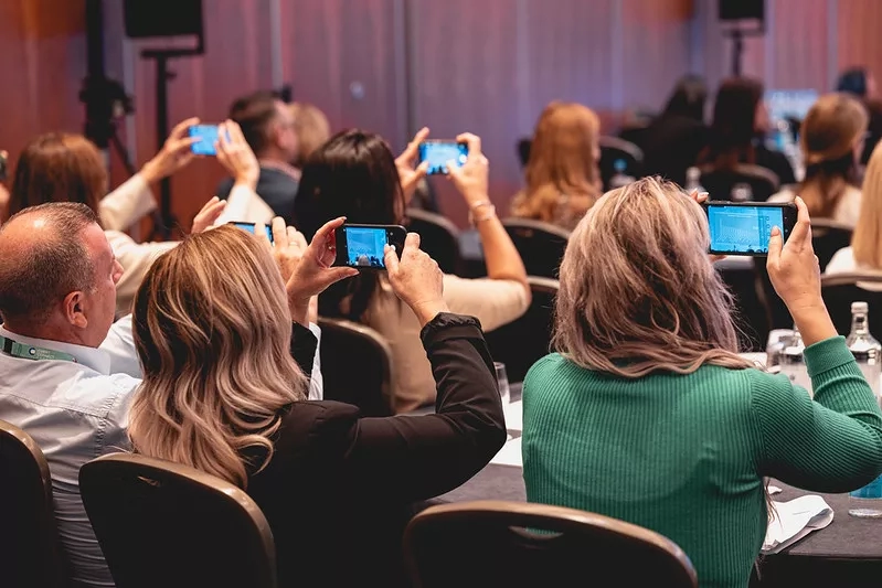 Group of people at a conference using smartphones to take pictures of the event.