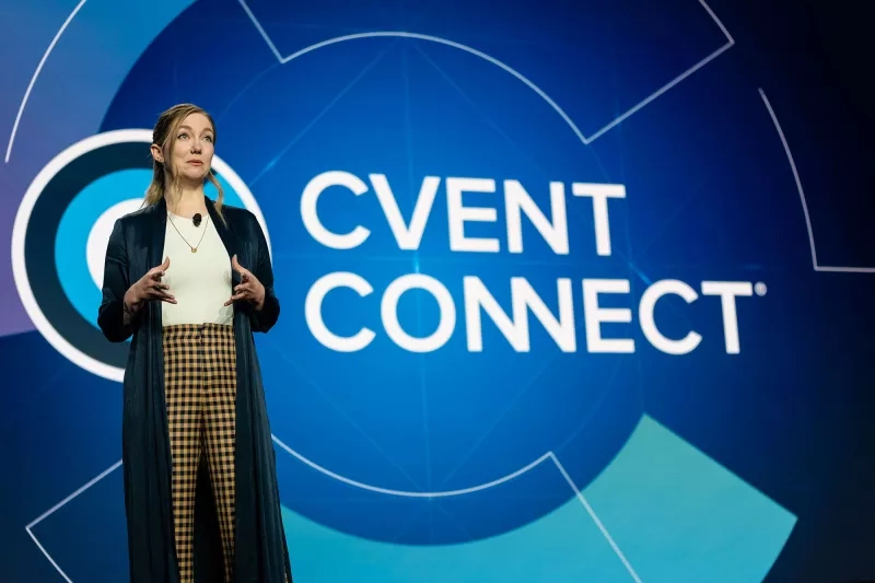 A woman in plaid pants speaks at Cvent Connect in front of a blue backdrop.