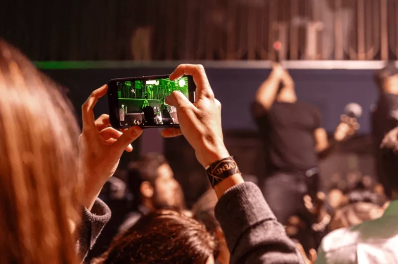 Person holding a phone up to film a concert at a venue in an image optimized for event SEO.