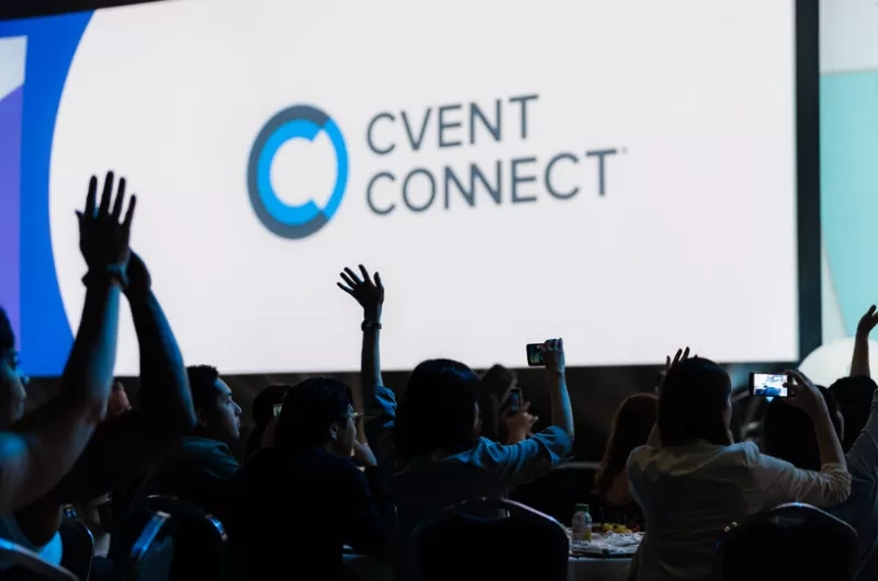A group of people are attending an event with a large screen displaying the Cvent Connect logo.