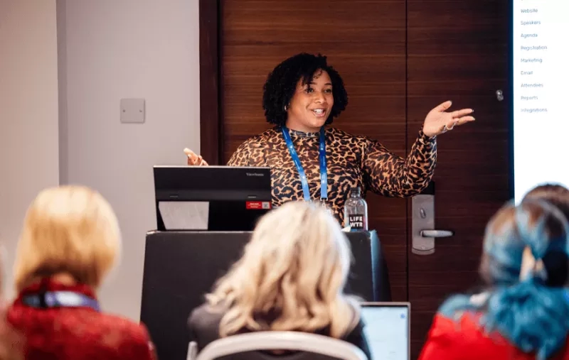 A lady with leopard print dress is giving a presentation to an audience.