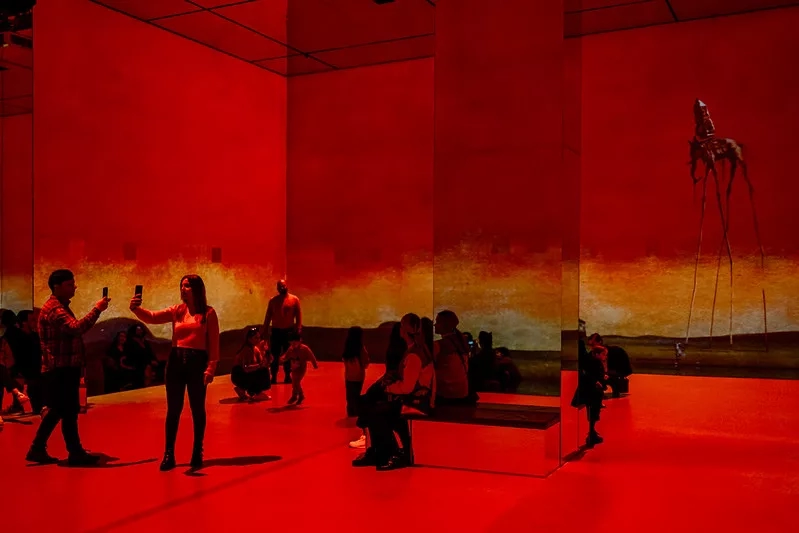 People inside the Dali museum, standing and taking pictures in front of the large red Dali mural.