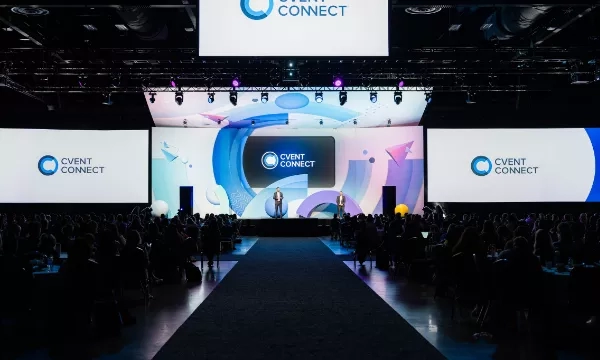 A large crowd is gathered for the Cvent Connect conference, with two speakers on stage and a large screen behind them.
