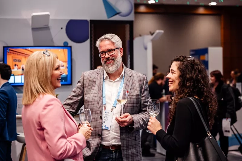 Two women and a man in a blazer talk with wine glasses at Cvent CONNECT Europe 2024.