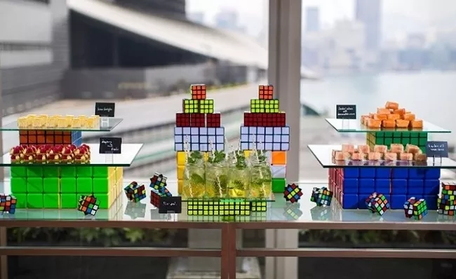 Rubik's cube themed table with a variety of snacks, drinks, and cubes on display.
