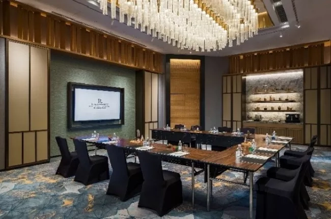 A conference room in The Ritz-Carlton, Bali, with long tables, chairs, and a chandelier.