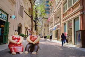 Two sculptures sit on Lee Tung Avenue in Hong Kong with stores in the background.