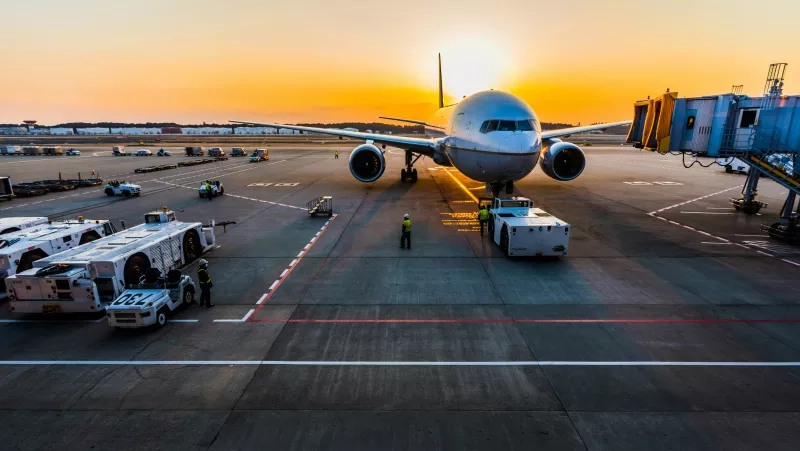 An airplane at the airport with service trucks and people at the runway at sunset.