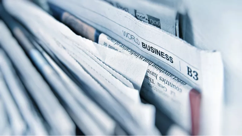 A newspaper titled "Business" is placed on top of other newspapers, and the image is slightly blurred.