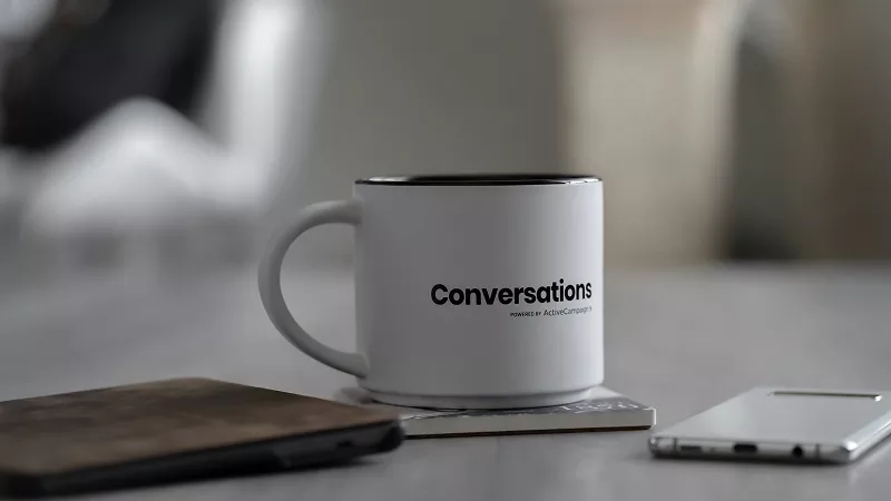 A mug with the word conversations on it next to a phone and a wallet.