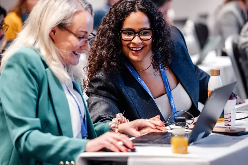 Two attendees at Cvent CONNECT Europe 2024 working together on a laptop at an event table.