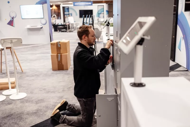 Man setting up Cvent CONNECT Europe 2024 event in a room with chairs, monitors, and boxes.