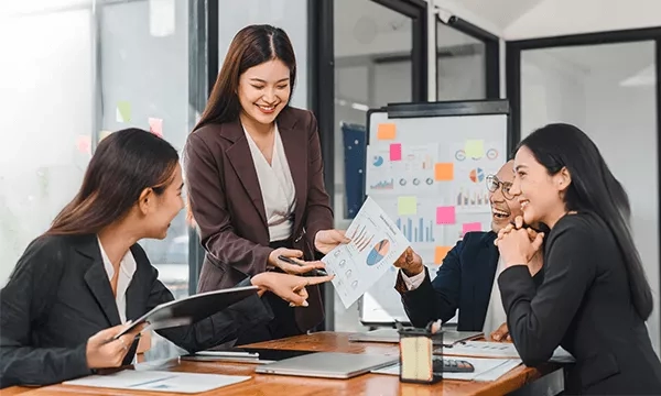 Four people having a meeting at a table with a woman in the middle talking to the others.