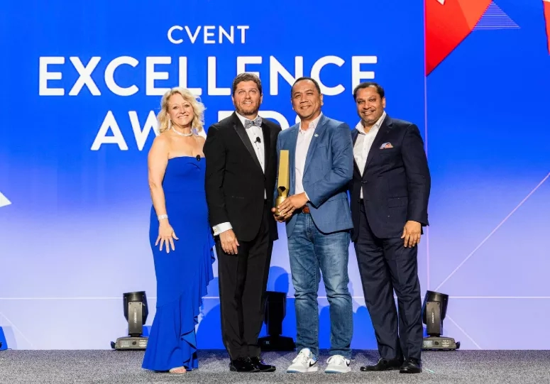 Four people posing for a photo with a trophy and text Cvent Excellence Award on a blue screen.