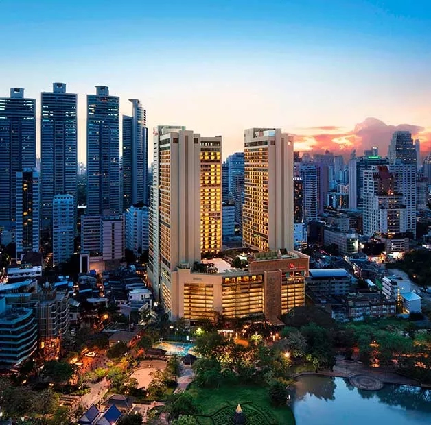 An aerial view of the Bangkok Marriott Marquis Queen’s Park with illuminated buildings and a sunset sky.
