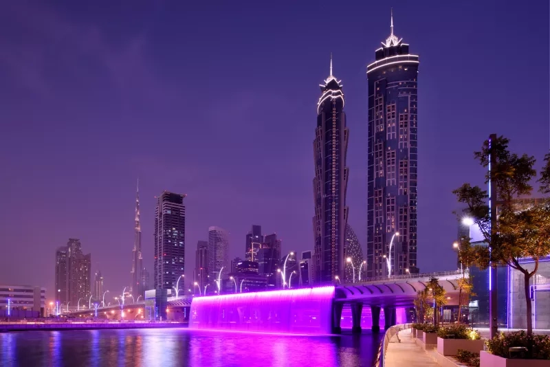 A cityscape at night featuring the JW Marriott Marquis Hotel Dubai, a bridge, and illuminated water.
