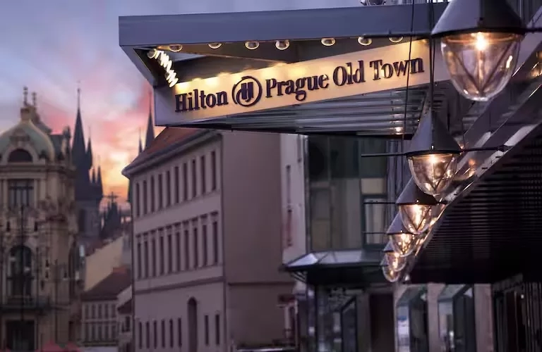 Exterior of the Hilton Prague Old Town hotel with a hotel name sign and lights hanging from the roof.