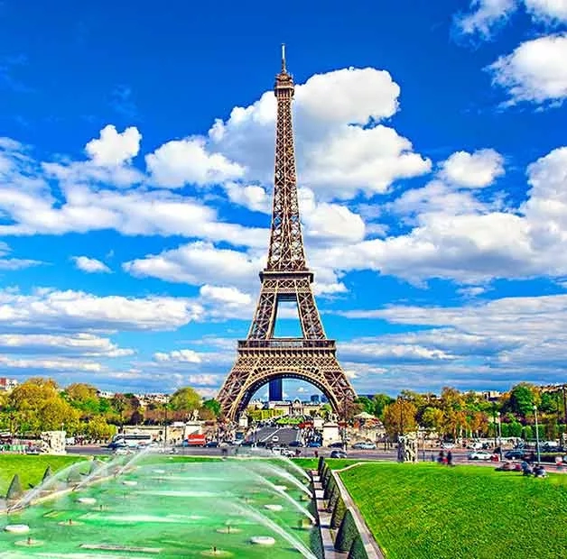 The Eiffel Tower in Paris, with a fountain and lush green grass, under a blue sky.