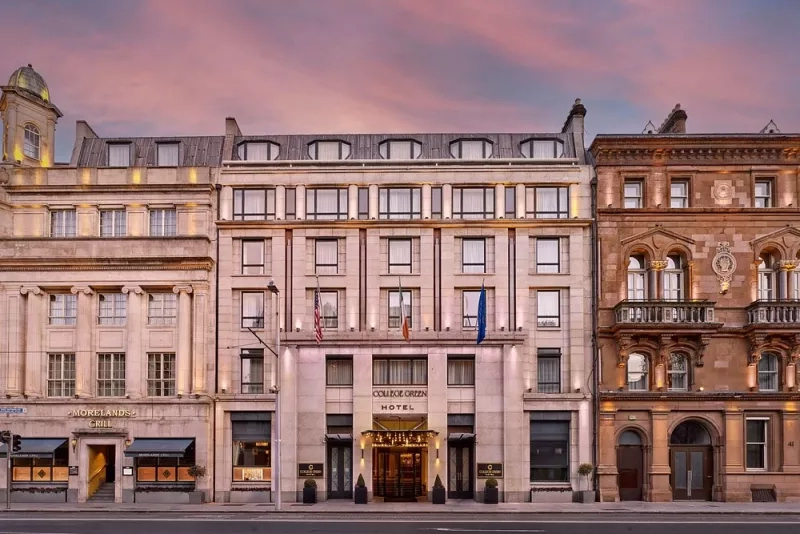 College Green Hotel Dublin, Autograph Collection facade at sunset with warm pink hues and lit up windows.