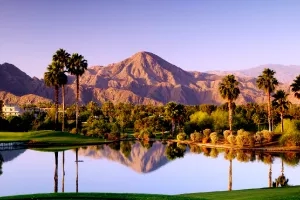 A serene landscape with mountains, palm trees, a reflective pond, and lush greenery at Indian Wells Golf Resort.