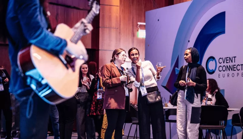 Event Connect Europe: Women gather, laughing, with wine glasses, while a guitarist plays in the background.