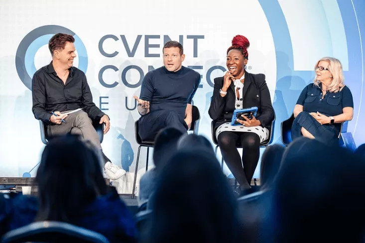 Four speakers sit on a stage with Cvent Conference written behind them and an audience sits in front.