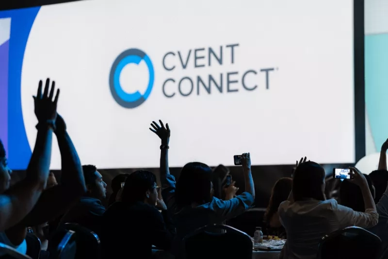 Audience with hands up in front of a screen with the Cvent Connect logo on it.
