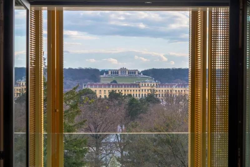 View from an open window of the Schönbrunn Palace with trees and hills in the distance.
