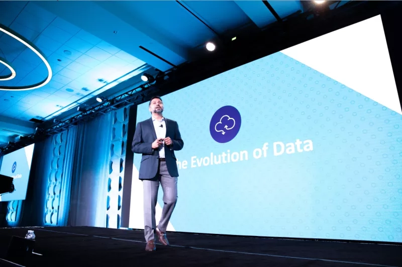 A man speaking on stage with the Evolution of Data logo behind him.