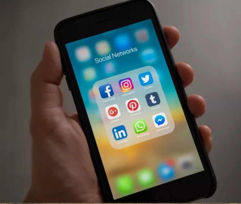 A person's hand holds a smartphone displaying various social media icons.