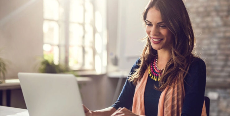 A smiling woman using a laptop at a desk in an office