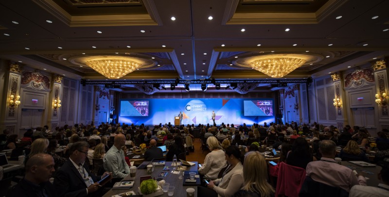 A large room with people sitting in chairs and a screen displaying "Cvent Connect" on it.