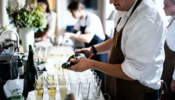 A man is pouring champagne into glasses at a gathering at Hotel Emma.