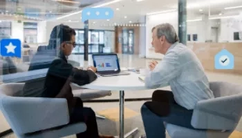 Two people are sitting on chairs facing each other and discussing something while a laptop is on the table.