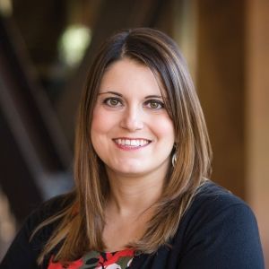 A headshot of a smiling woman with brown hair and wearing a blue shirt and colorful shirt.