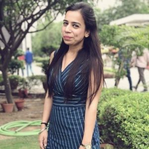 Megha Jetley is standing in the garden area with a green hose on the left side.