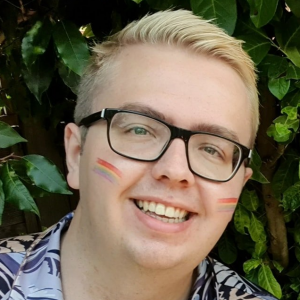 A portrait of a man with rainbow paint on his face and wearing glasses.