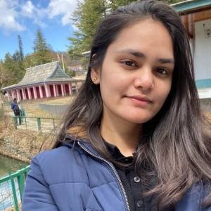 Portrait of Saumya Chaudhary against a serene landscape featuring a pink temple and lush greenery.