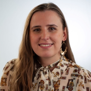 Olivia Cal headshot of her smiling with long hair and wearing a patterned shirt with a white collar.