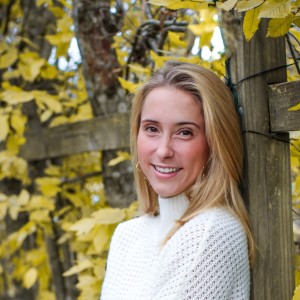 A woman smiling with yellow leaves and a fence in the background.