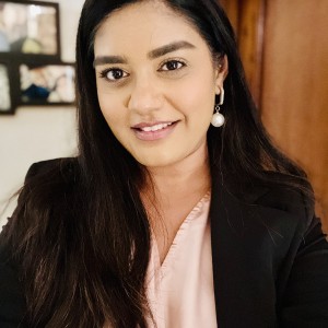 Woman with long black hair wearing a pink shirt and black blazer smiling at the camera.