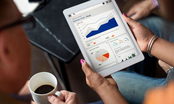 A woman is holding a tablet with a business chart and a cup of coffee.