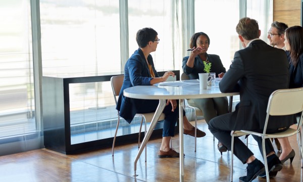 Five people sitting around a table in a conference room with large windows and a TV.
