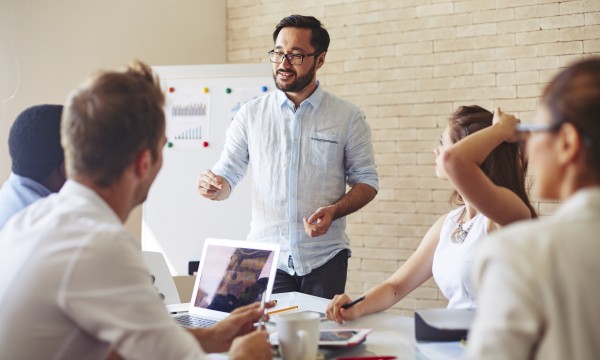 Man standing and giving a presentation to a group of people in an office meeting room.