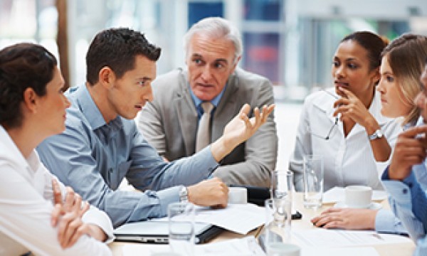 A group of people in formal attire sitting around a table in a meeting discussing something.