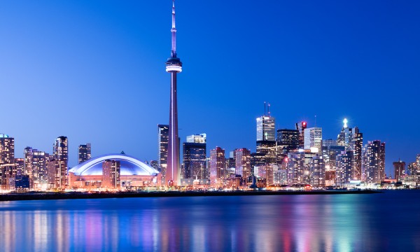 A beautiful picture of Toronto's skyline at night with colorful reflections on the water in front.