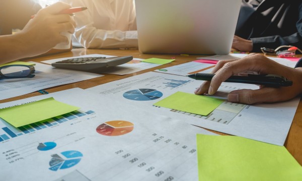 Group of people in a meeting with papers, pens, and a laptop on the table.
